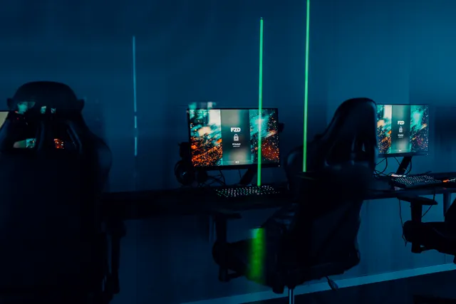 Datorskärmar och gamingstolar i ett mörkblått rum