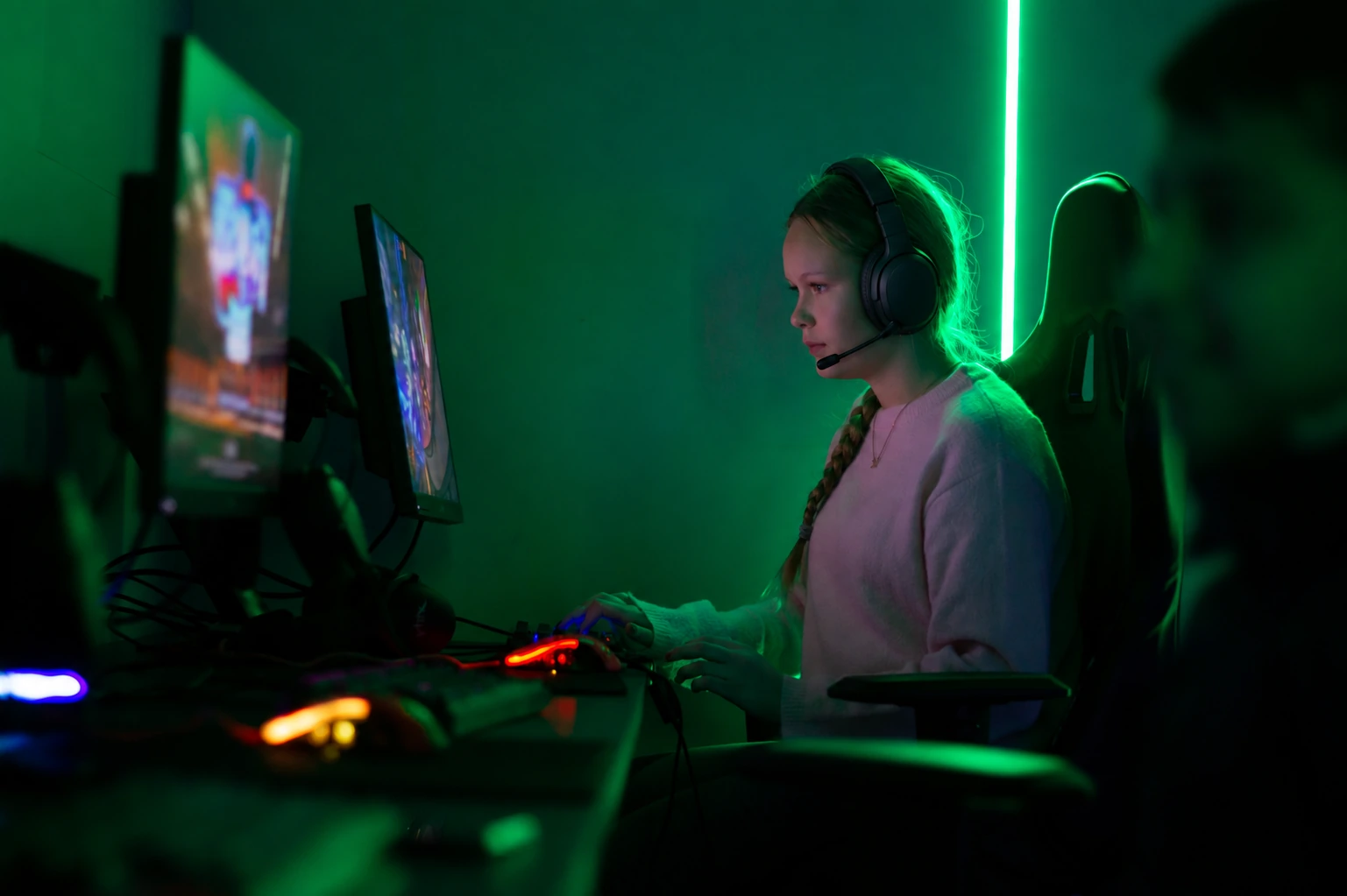 En ung spelare med gamingheadset vid en dator i ett grönbelyst spelrum på FUZED